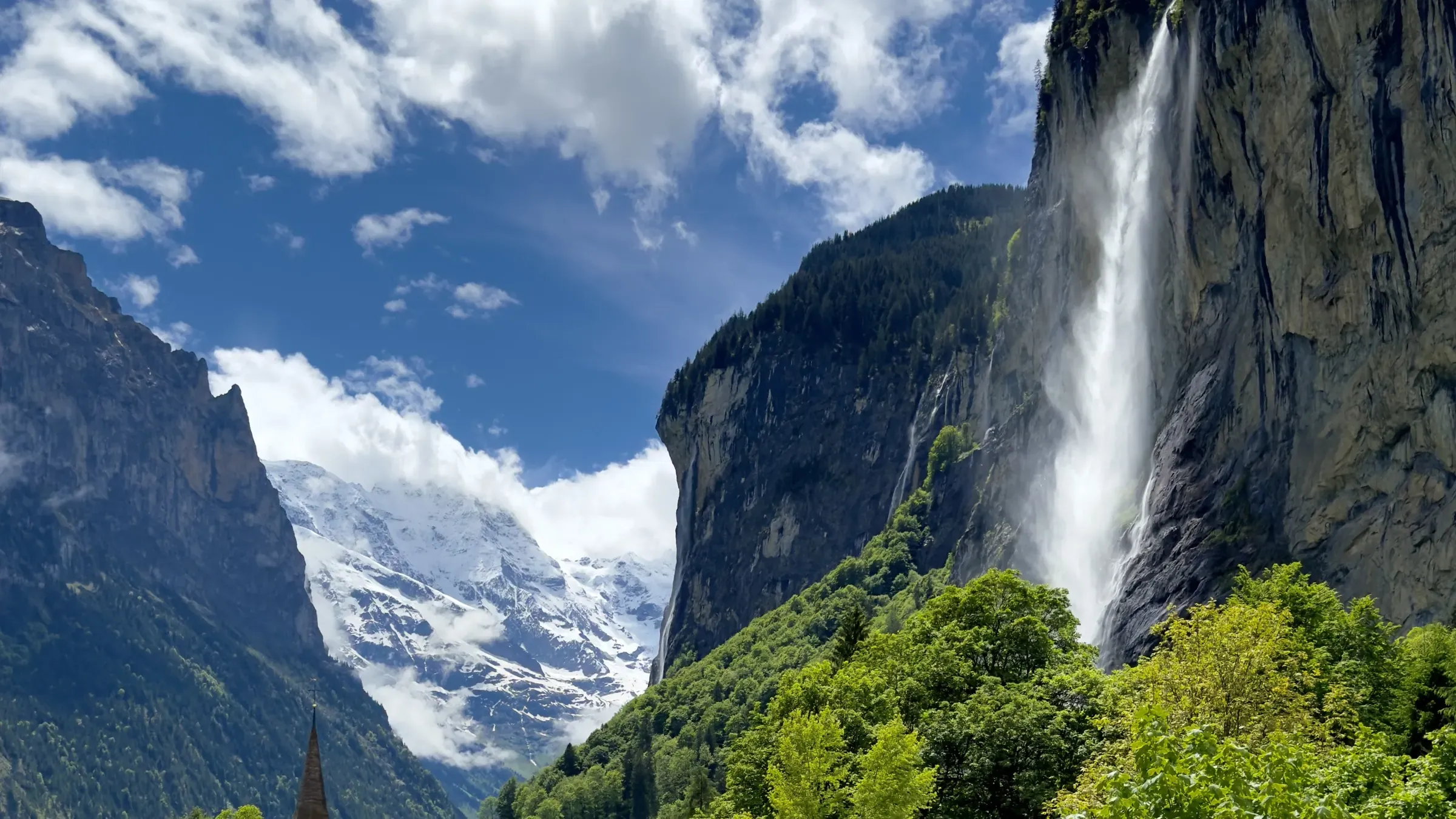 Staubbach Falls dropping behind the village church in Lauterbrunnen, under a blue sky full of clouds
