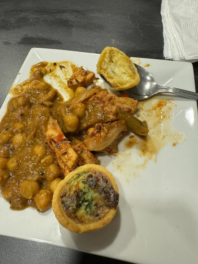A plate of curry, chickpeas and a small spinach quiche at the airport lounge