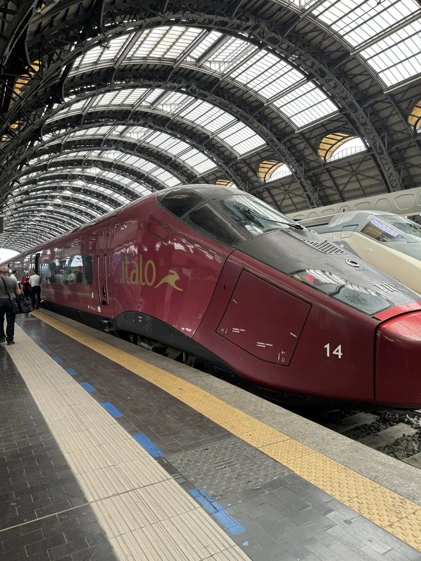 The red Italo high-speed train at platform 14 under the arched iron roof of Milano Centrale