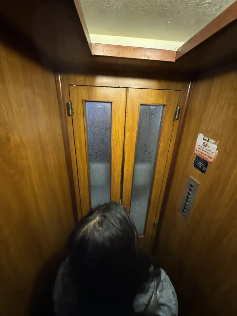 Arsha facing the folding wooden doors of a very old, very small elevator