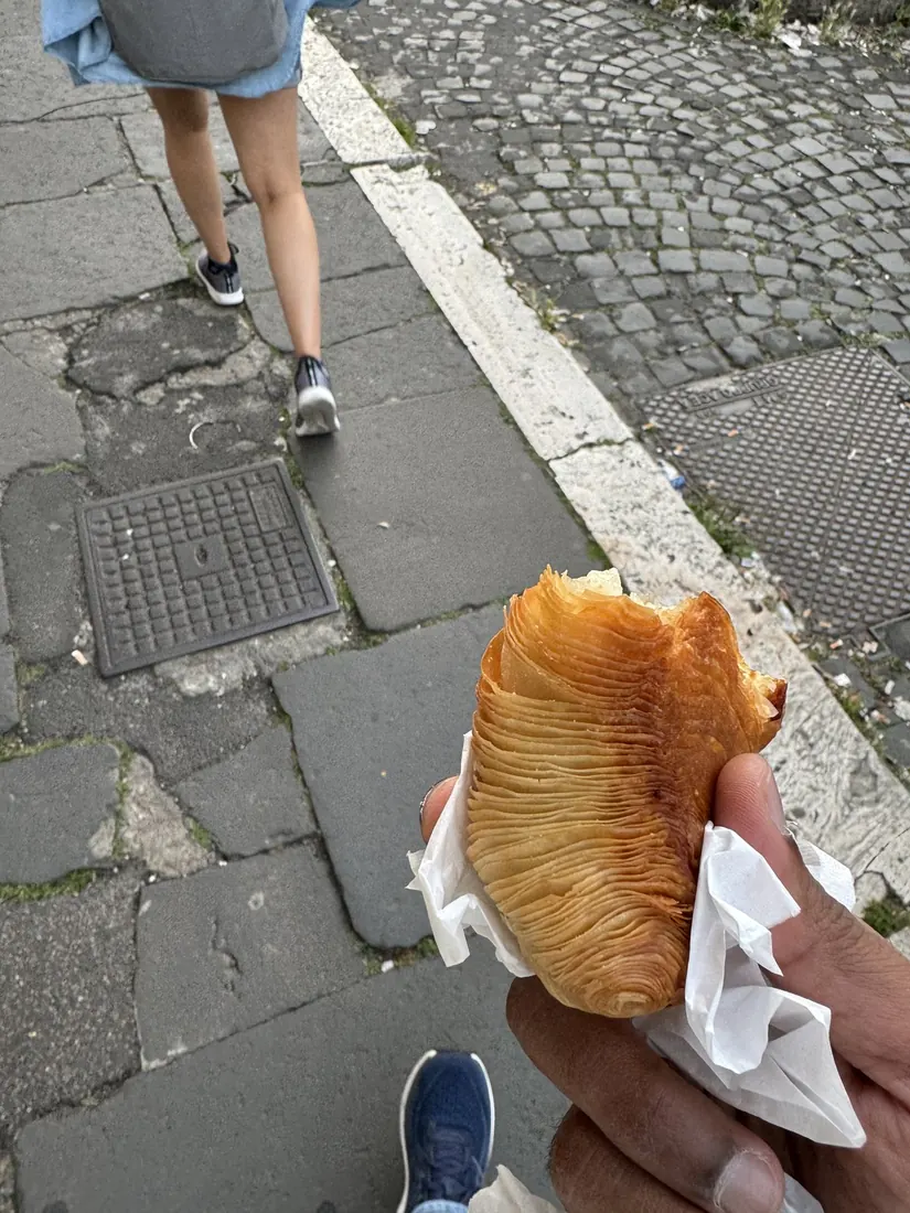 A shell-shaped sfogliatella pastry with one bite missing, held up on a Roman street
