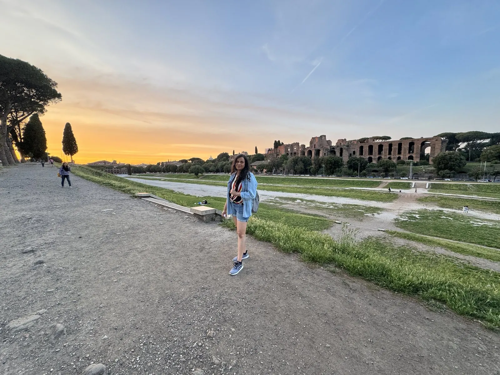 Arsha walking along the edge of the Circus Maximus at sunset, the ruins of the Palatine glowing behind her