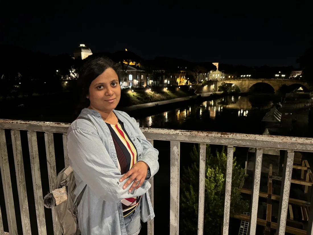 Arsha on a bridge over the Tiber at night, the river and lamps glowing behind her