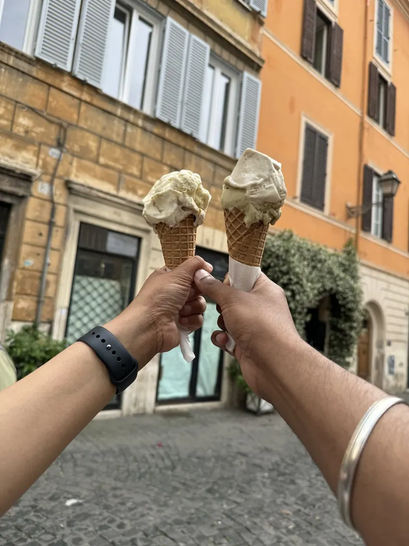Two hands holding up two gelato cones on a Roman street