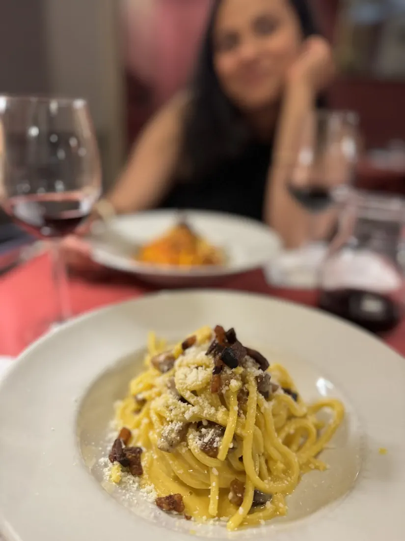 A plate of carbonara with crispy guanciale, Arsha blurred in the background