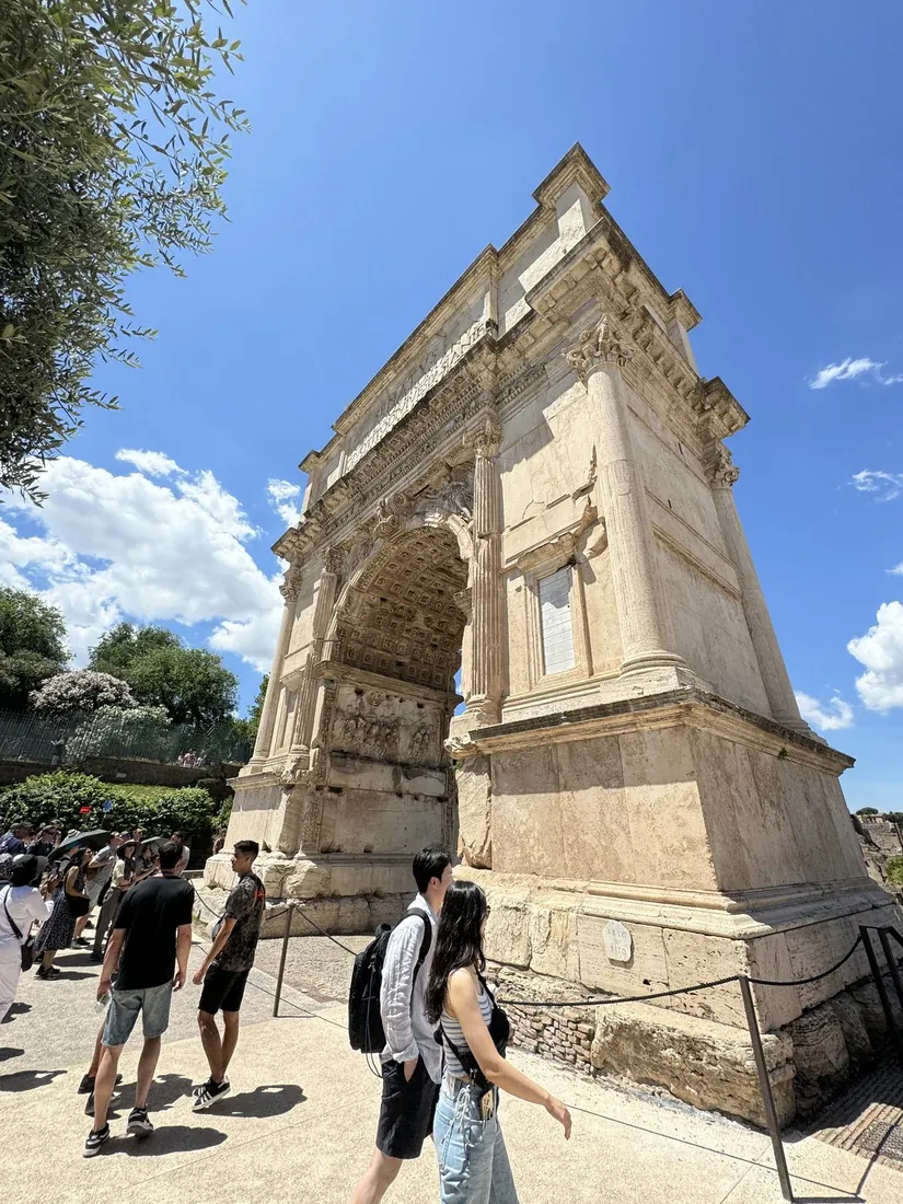 The Arch of Titus against a blue sky, visitors walking beneath it