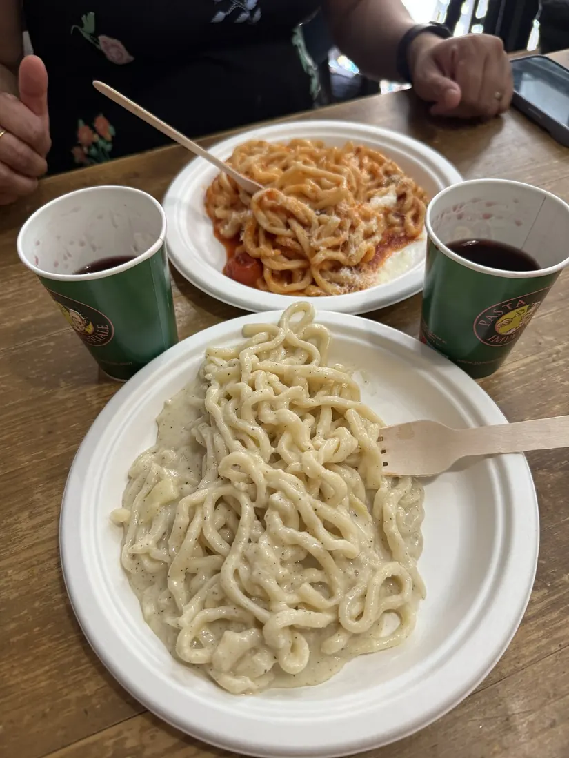 Fresh pasta on paper plates with red wine in paper cups on a wooden counter