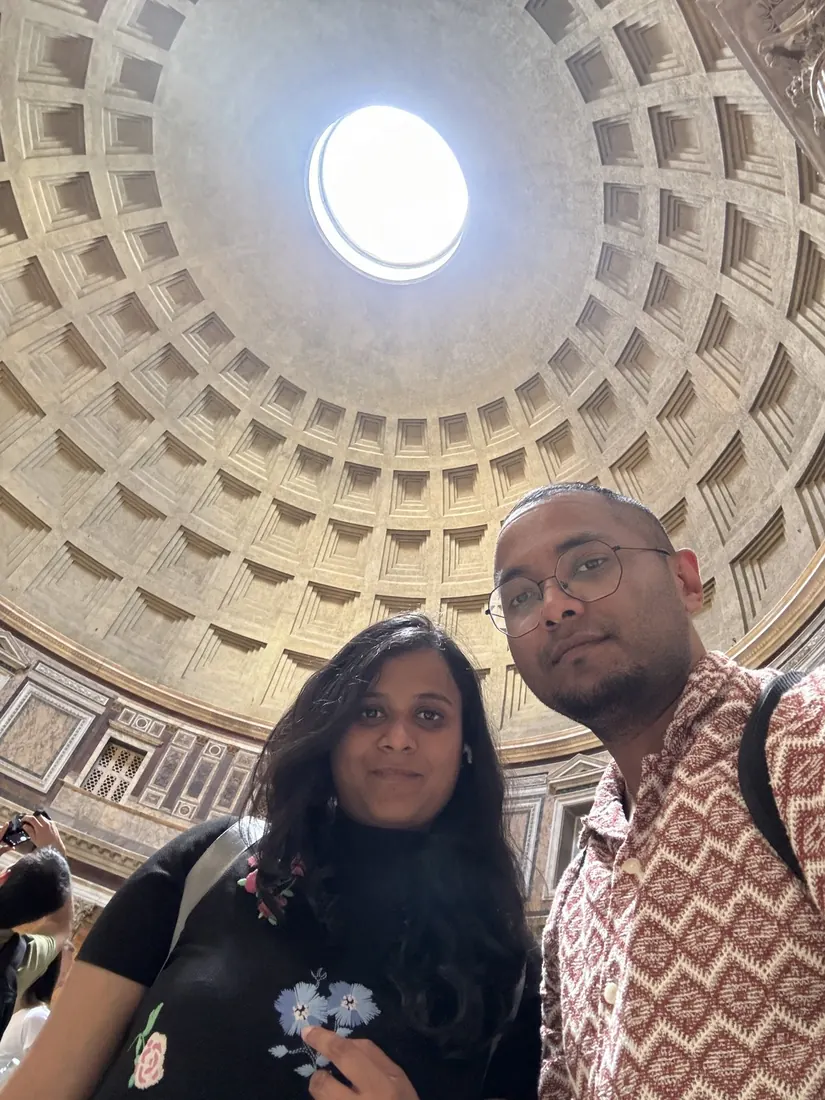Arsha and Binu taking a selfie under the Pantheon's coffered dome, the bright oculus above them