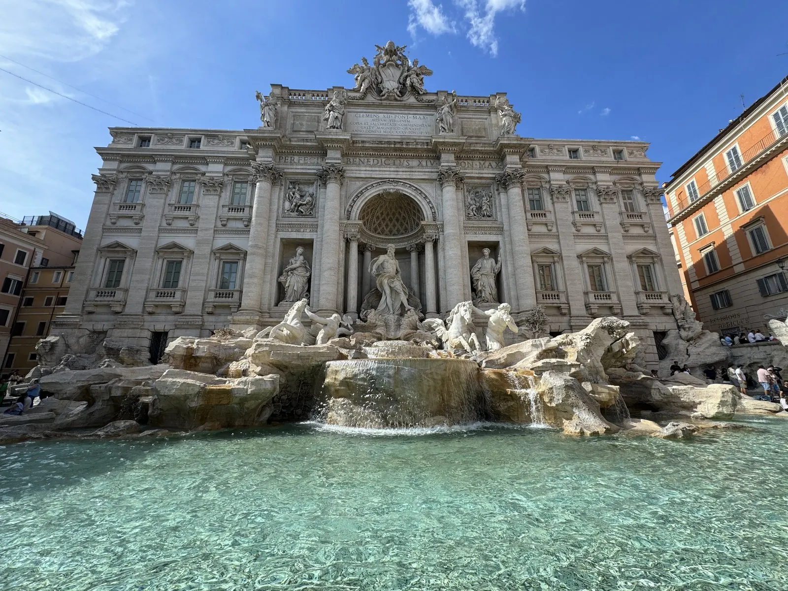 The Trevi Fountain in full sun, turquoise water in front of the white palace facade and its statues