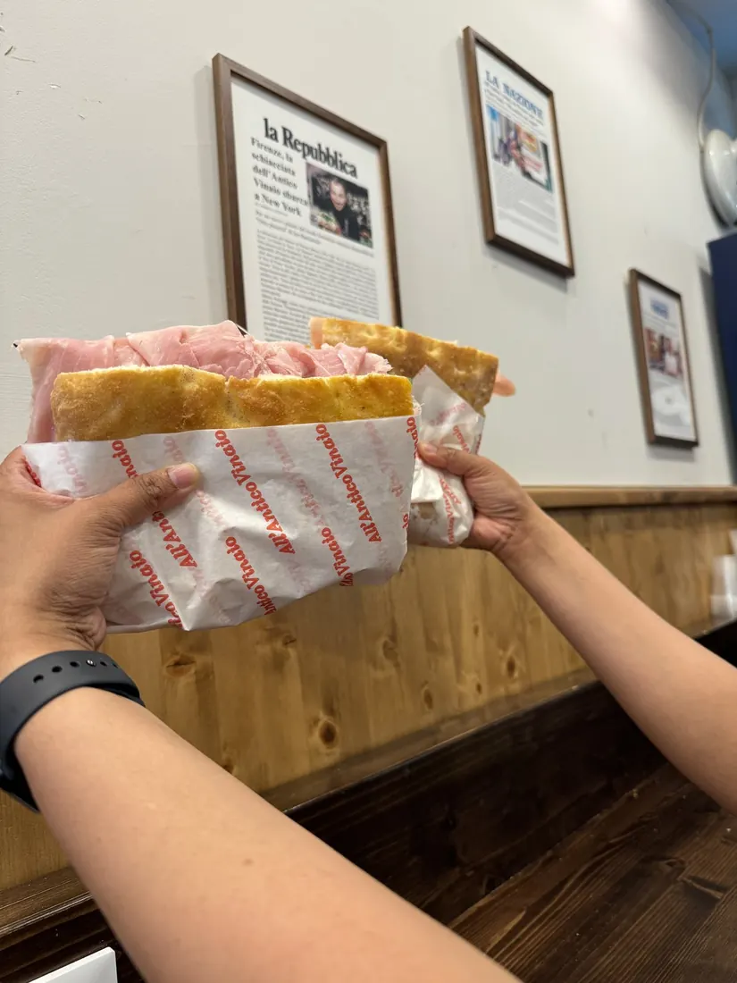 Two hands holding up schiacciata sandwiches in paper wrappers