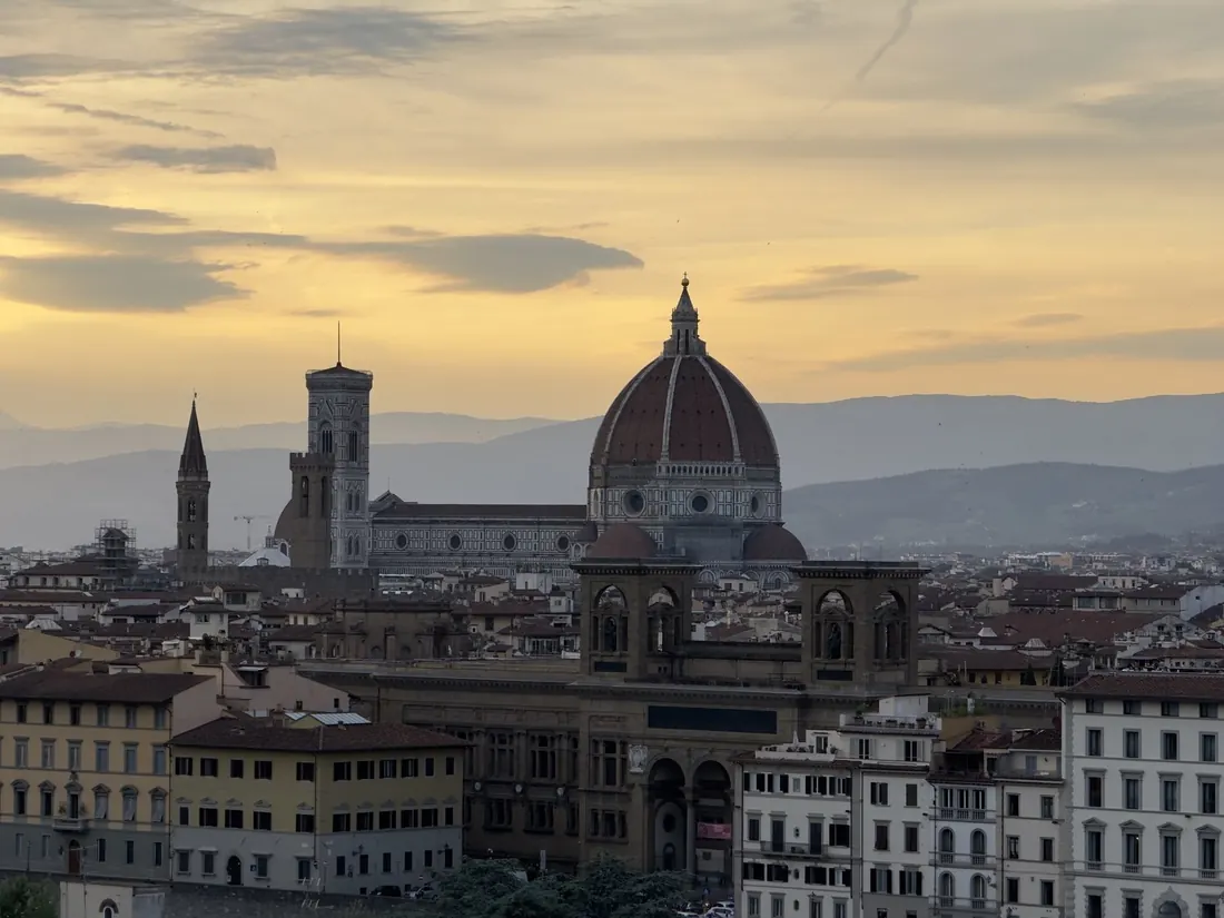 The Duomo and Palazzo Vecchio tower against a gold and grey sunset sky