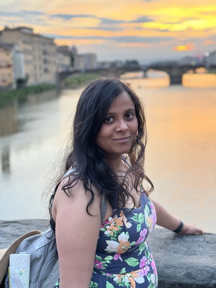 Arsha by the river wall, the Arno and a bridge glowing in the sunset behind her