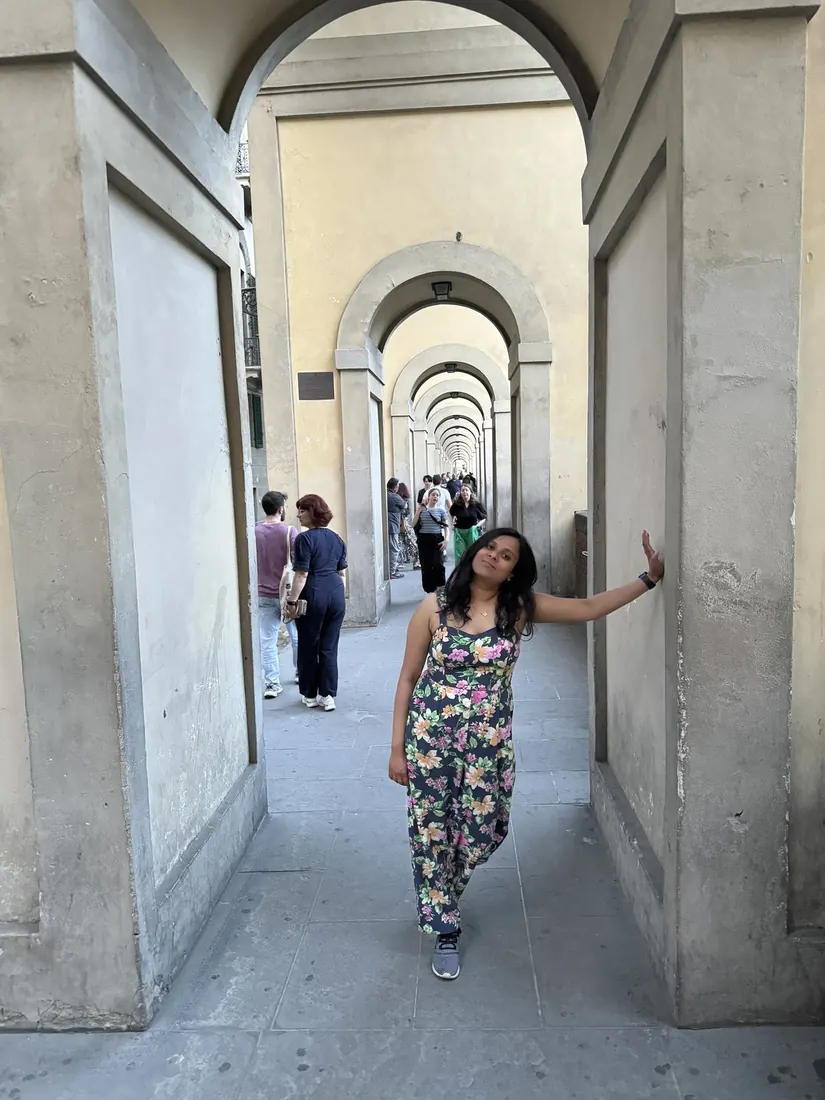 Arsha in a long stone arcade by the Uffizi, the arches repeating behind her