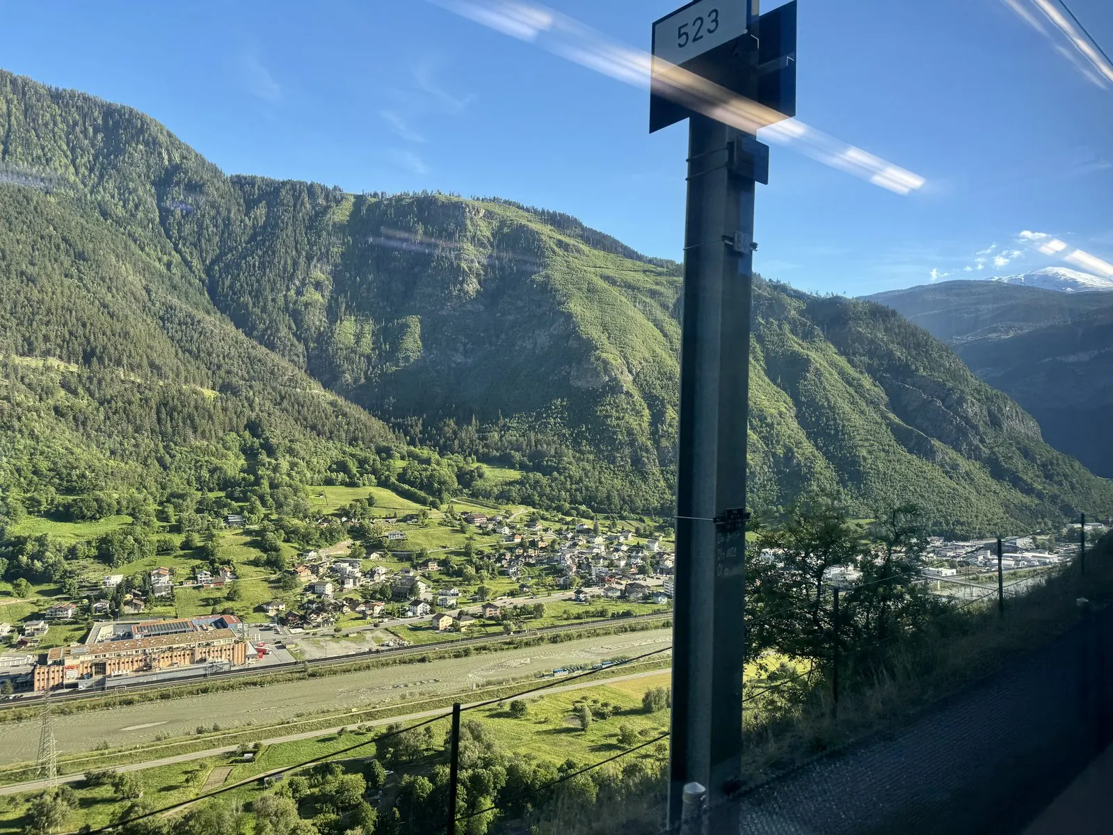 A green Swiss valley with villages and steep mountains seen through the train window