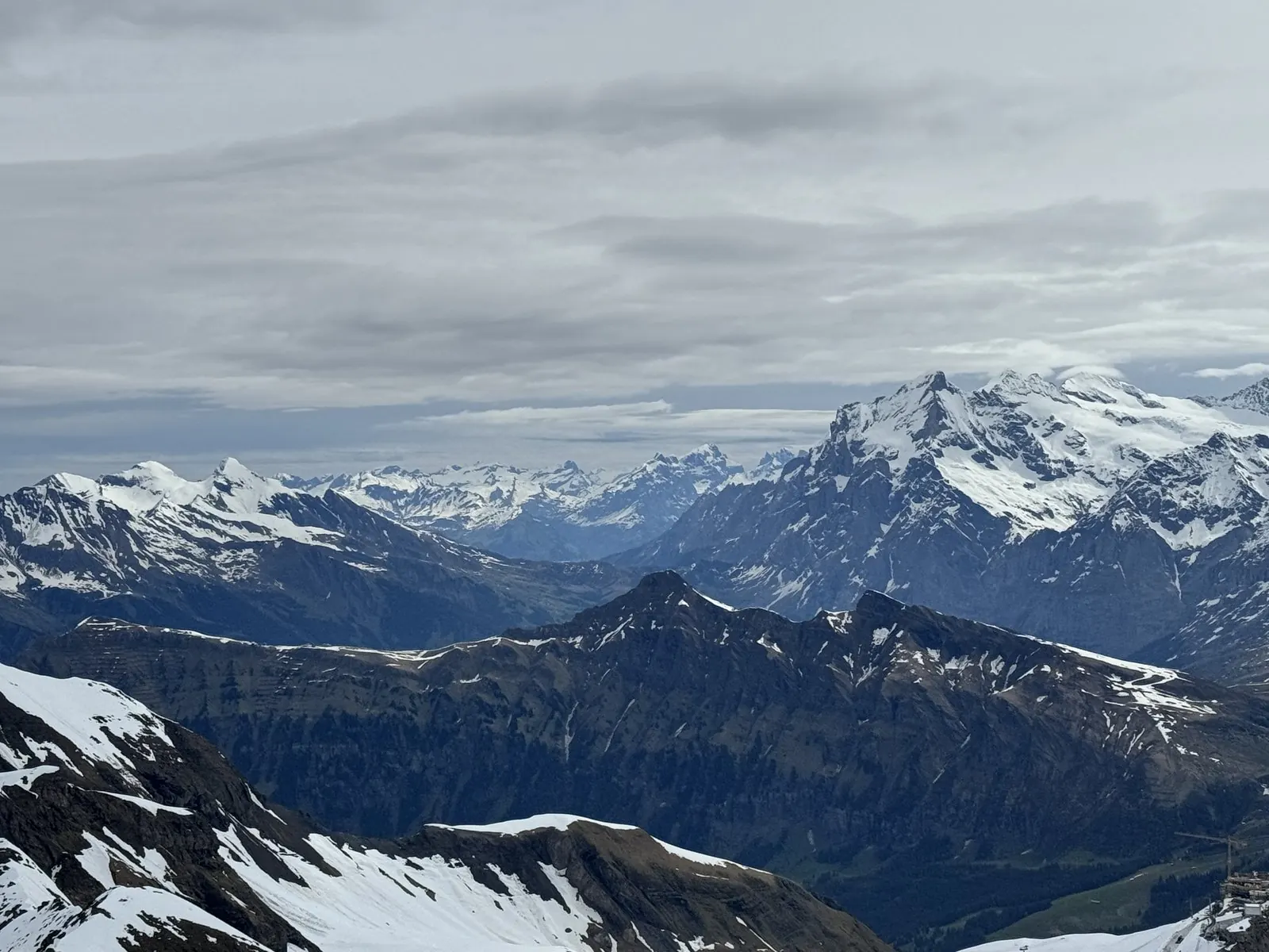 Snow-dusted Alpine peaks and valleys seen from the Schilthorn summit under a grey sky