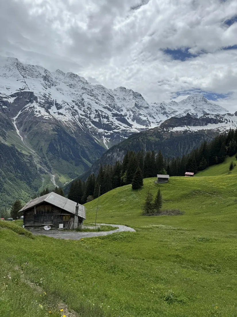 A wooden hut on a green meadow below snowy mountains