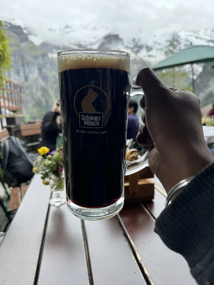 A glass of dark Schwarzmönch beer held up at an outdoor table in Gimmelwald