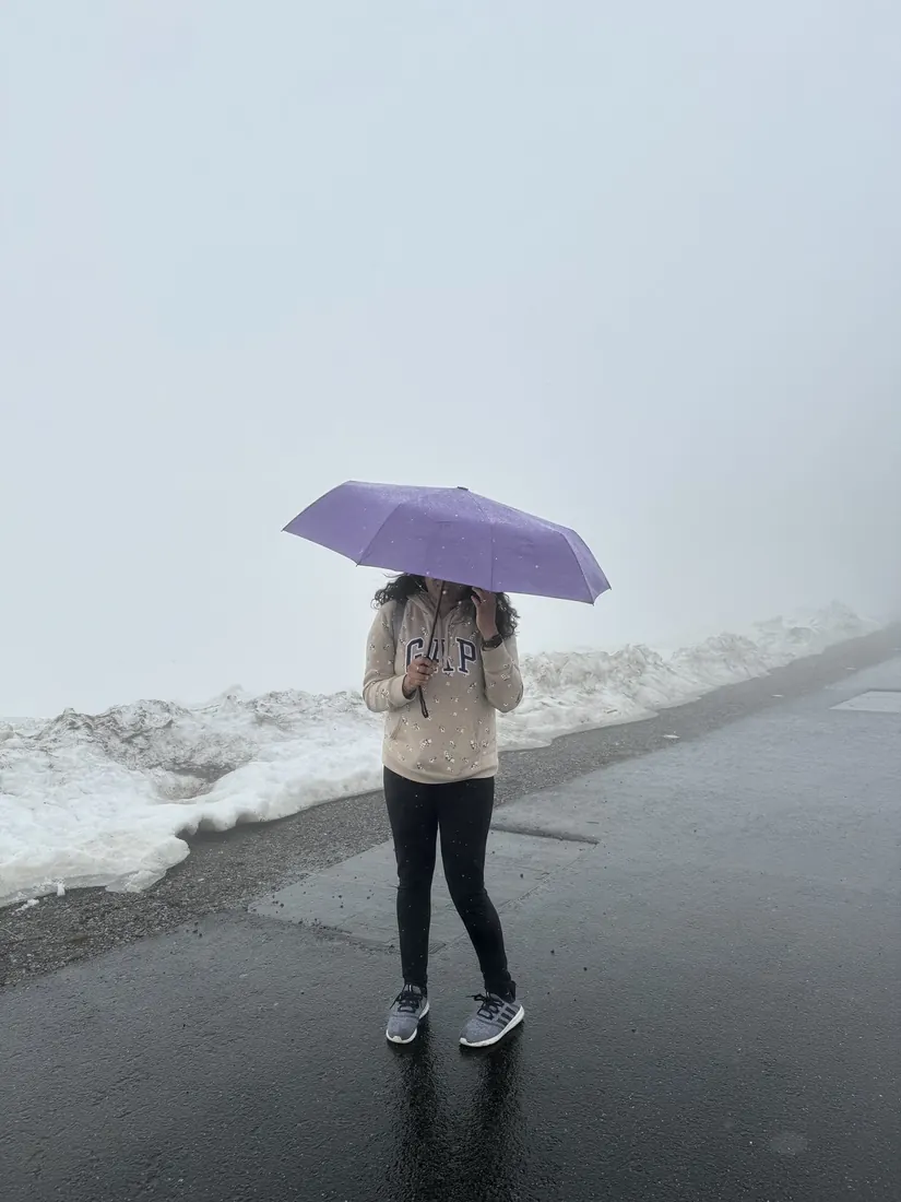 Arsha under a purple umbrella on a foggy ridge path with patches of snow
