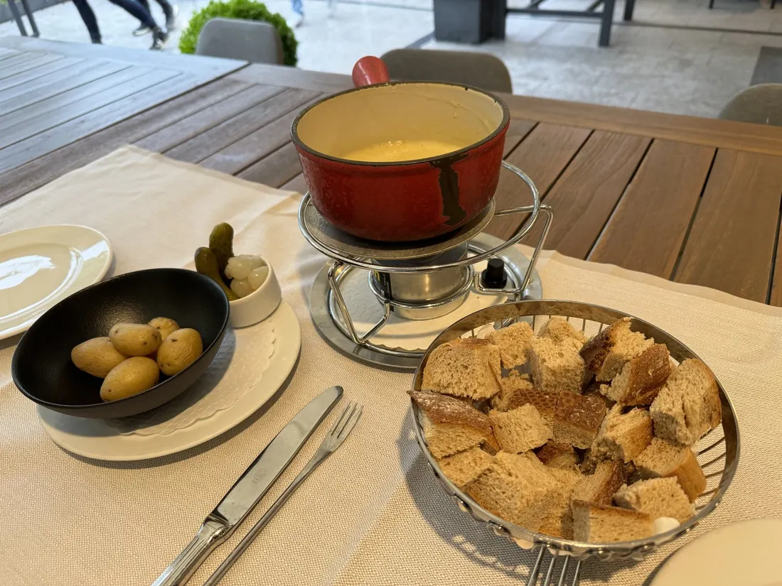 A pot of cheese fondue with a basket of bread cubes and pickled onions on a restaurant table