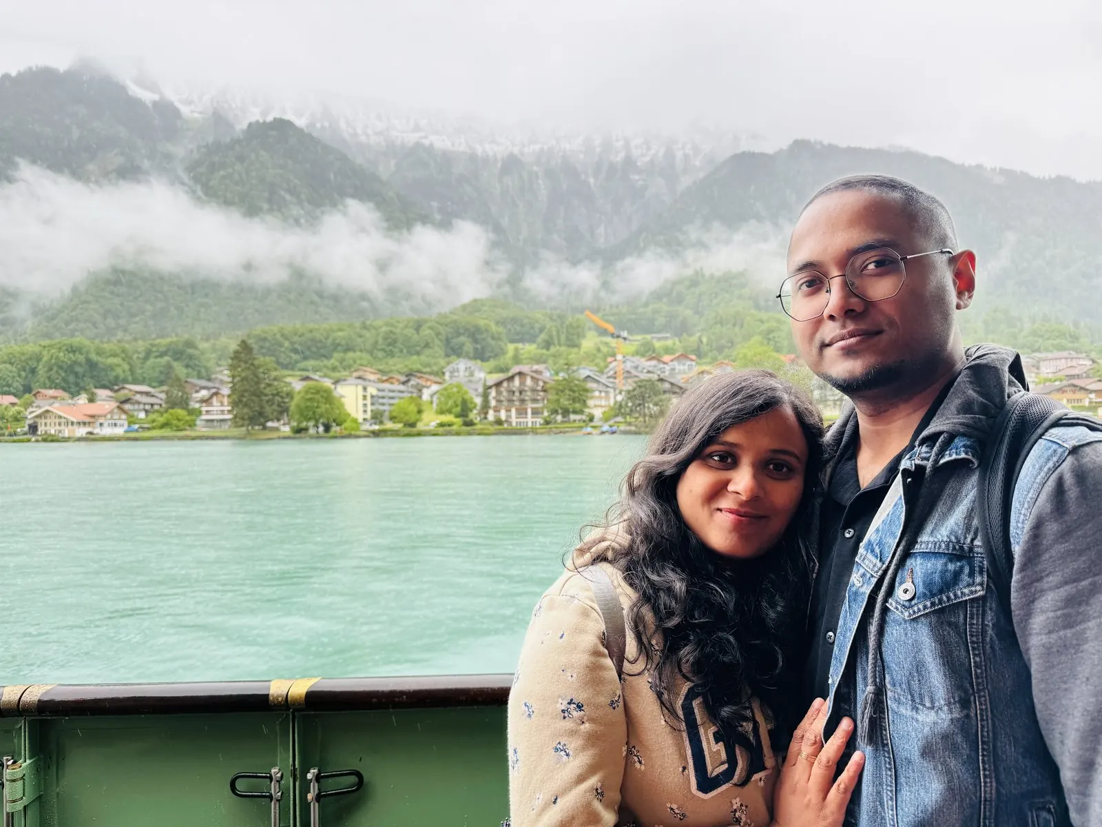 Arsha and Binu on the Lake Brienz boat deck, milky turquoise water and cloud-wrapped mountains behind