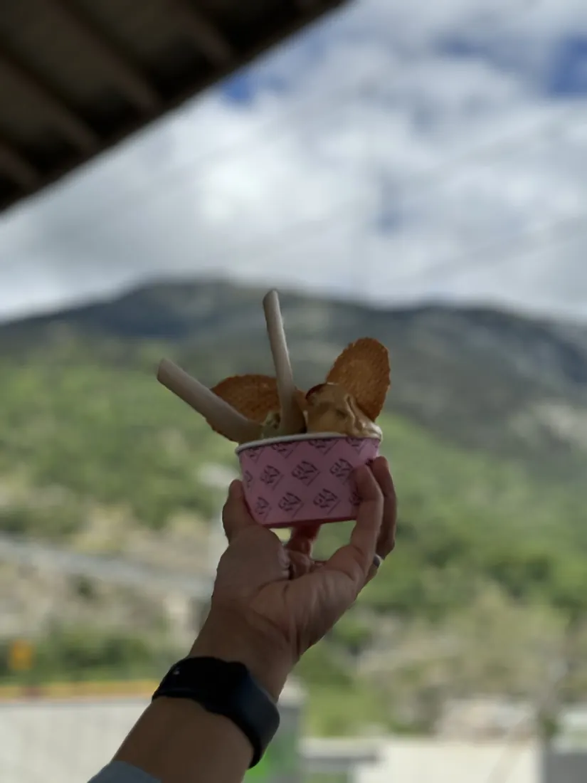 A pistachio gelato held up against a mountain backdrop at Brig station