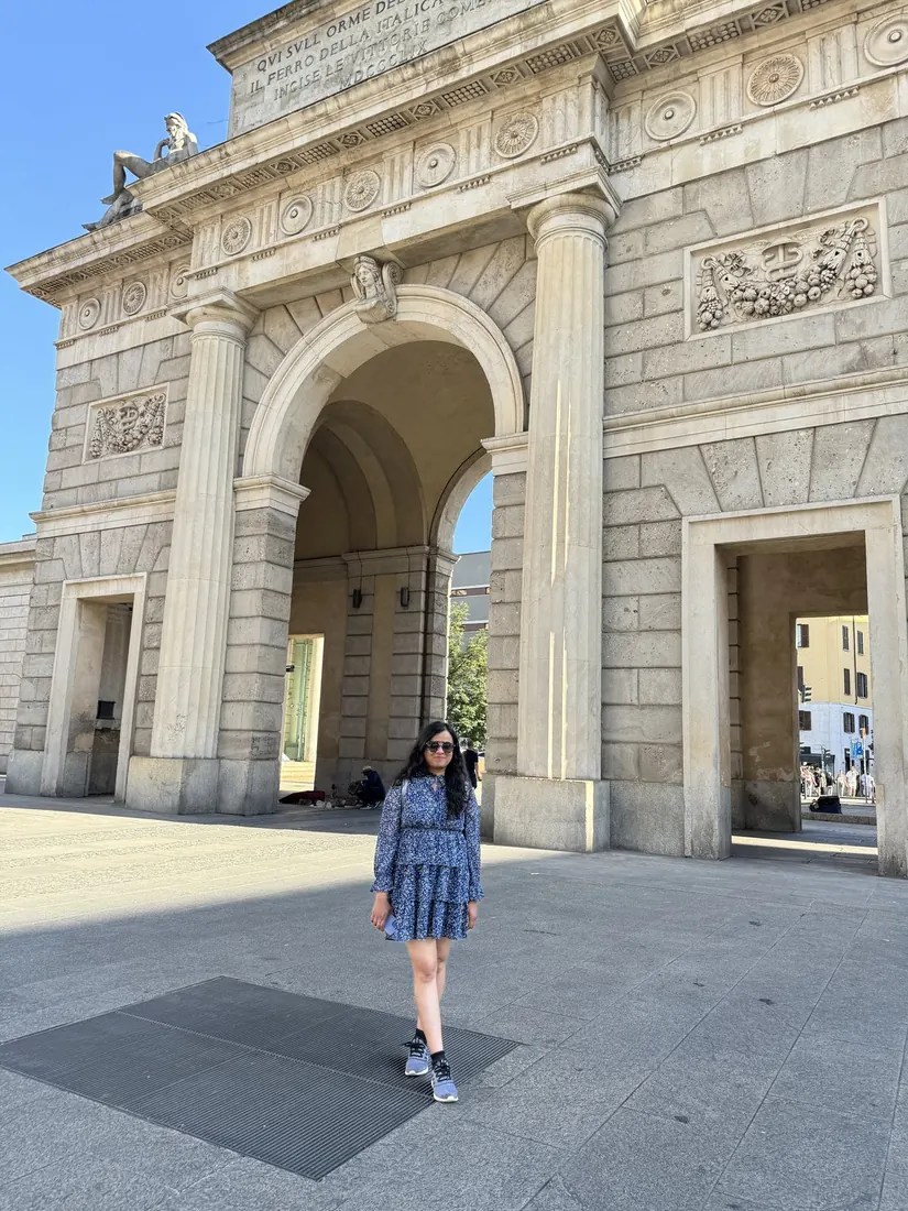 Arsha walking under a grand stone triumphal gate