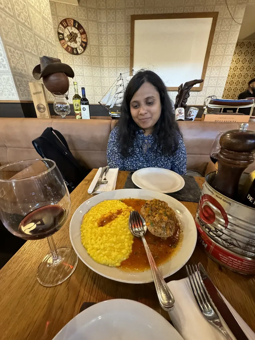 Arsha at a restaurant table behind a plate of saffron risotto and ossobuco