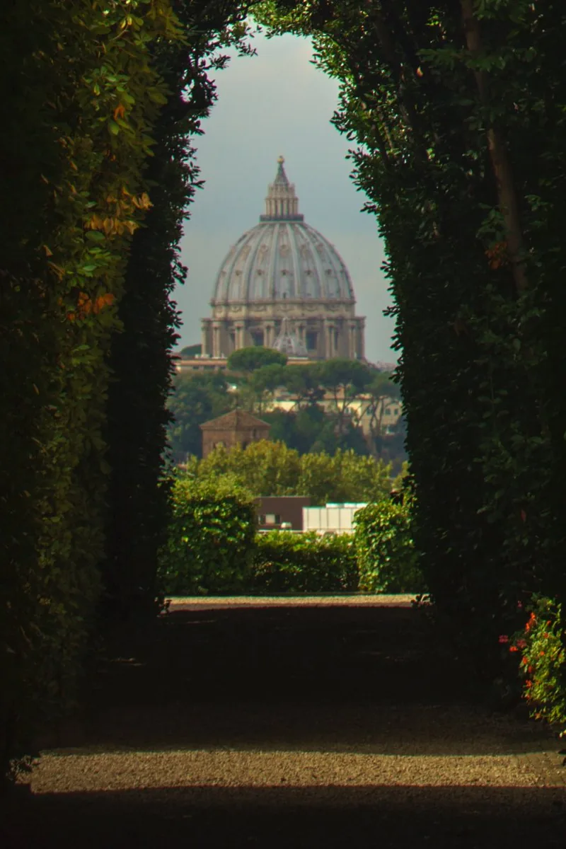 St. Peter's dome framed at the end of a dark tunnel of hedges, seen through the keyhole on the Aventine