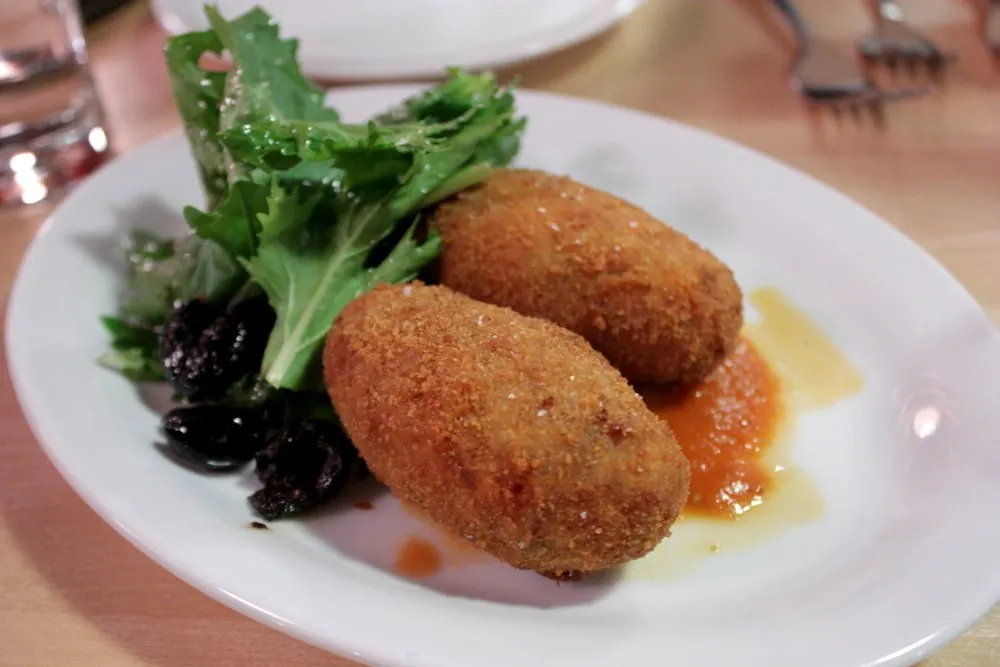 Two supplì on a white plate with salad leaves