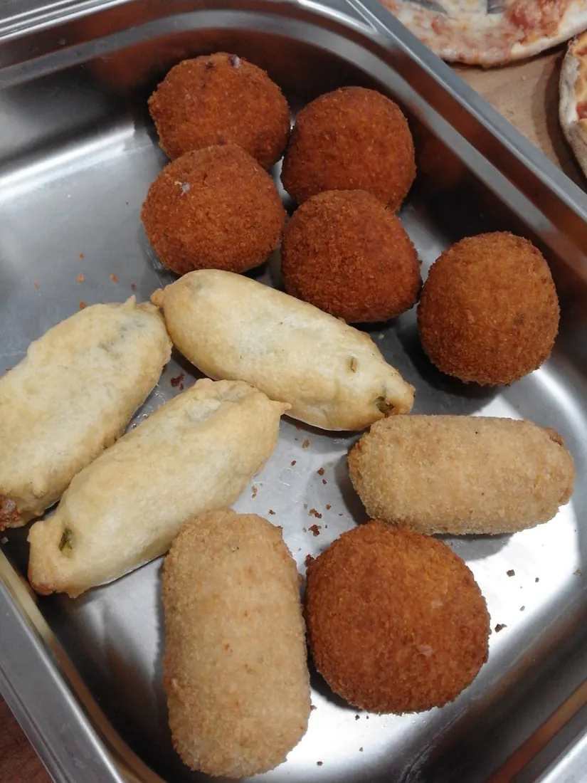 A steel tray of assorted supplì, some round and dark, some long and pale